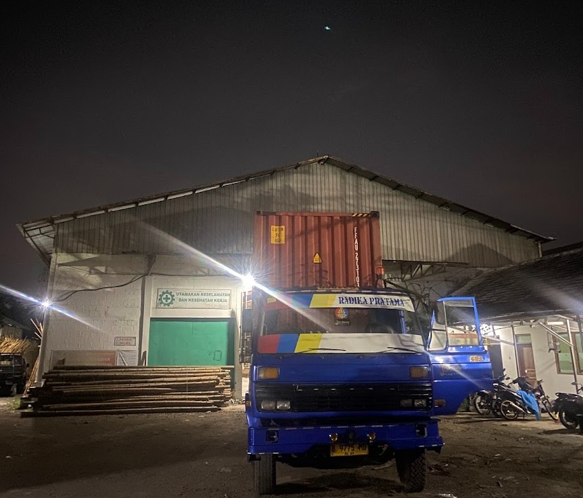 Late-night dispatch — export container mounted on a Radika Pratama truck outside the warehouse